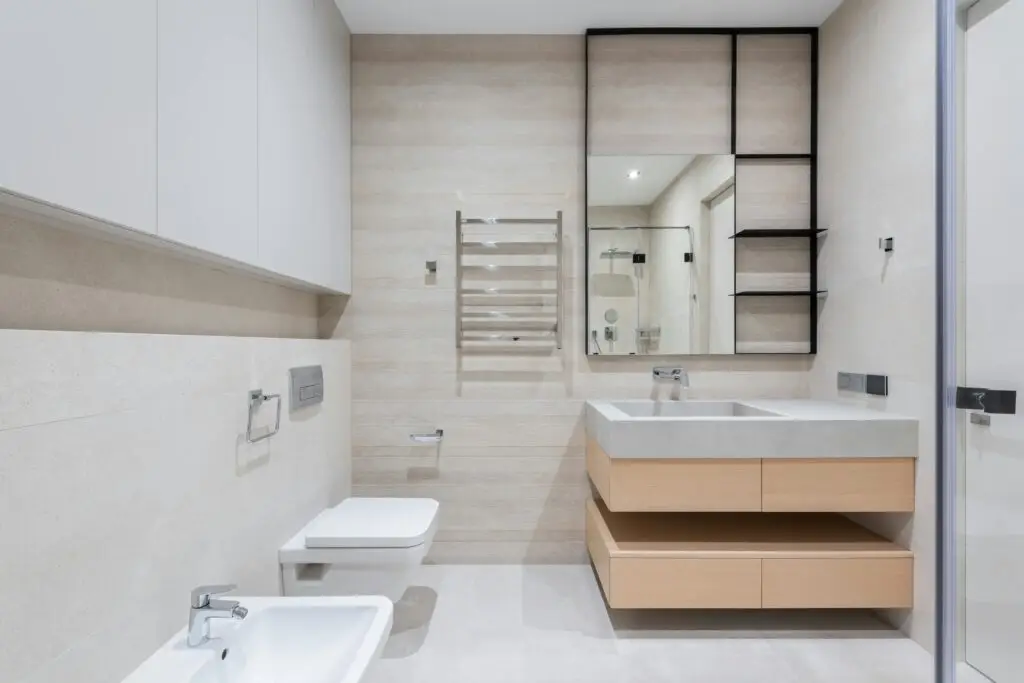Interior of modern light bathroom with bidet and toilet next to sink with cabinet under mirror